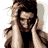 A pixelated static image of a person with long dark hair wearing a light-colored jacket over a black top, hands raised near the head.