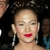 A pixelated close-up of a person with dark hair, red lips, and dangling earrings against a dark background.