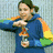A person in a blue hoodie with rainbow sleeves holds an object, then drinks from it while turning their head right.