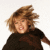 Pixelated image of a person with light brown hair wearing dark clothing against a white background.