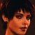 Pixelated close-up of a person with dark hair and light skin, showing partial face and shoulder against dark background.
