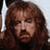Pixelated close-up of a person with long brown hair and a mustache, wearing dark clothing against a light background.