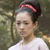 A static pixelated image shows a person with dark hair tied back by a red headband, wearing a white top against a blurred greenish background.