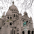 Pixelated image of a domed building with multiple towers and arched windows, set against a light background.