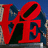 Red 'LOVE' sculpture with blue background, red text 'I', 'LOVE', and 'AMBER' on black field.