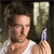 A person with short brown hair wearing a white tank top holds a small purple object near a large light-colored cylindrical item against a dark background.