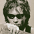 Pixelated grayscale image of a person with dark hair and sunglasses wearing a light-colored shirt against a neutral background.