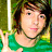 Pixelated image of a person with short brown hair wearing a green top and black choker, holding up two fingers in front of a blurred background.
