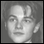 Grayscale pixelated portrait of a person with short hair, neutral expression, and visible facial features including eyes, nose, mouth, and ears against a solid gray background.
