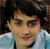A pixelated close-up of a person with dark hair wearing a light blue shirt against a dark background.