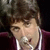 Pixelated close-up of a person with brown hair wearing a dark purple jacket over white shirt, static image.