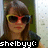 Pixelated image of a person with brown hair wearing yellow and red sunglasses, standing against a green wall with light-colored background.