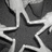 A grayscale pattern of interlocking star shapes with white outlines on a dark gray background, arranged in a repeating