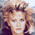 Static pixelated image of a person with curly light brown hair and closed eyes, wearing dark clothing against a blurred background.