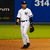 A baseball player in a white uniform walks across a field with a blue outfield wall displaying "314" and a black advertisement