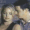Two people in a close embrace, one with dark hair and the other with light hair, both wearing casual clothing against a blurred background.