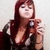 A pixelated image of a person with long dark red hair wearing a dark low-cut top, holding a small object near their face against a light background.