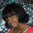 Pixelated image of a person with voluminous dark hair wearing red clothing against a patterned background.