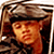 Pixelated static image of a person wearing a dark hat with light-colored brim, visible face showing warm-toned skin and closed eyes, set against a brownish background with indistinct shapes.