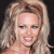 Pixelated close-up of a person with light brown hair styled in voluminous waves, wearing a strapless top against a dark background.