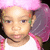 A pixelated close-up of a person with light skin wearing a white shirt and pink headwear, set against a dark background.