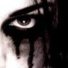 Close-up of a stylized eye with dramatic black makeup and dark liquid dripping from the lower eyelid against a light background.