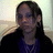 Pixelated static image of a person with long dark hair wearing a dark jacket over a blue shirt against a light background.