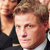 Pixelated close-up of a person with light brown hair wearing a dark suit and white shirt, cropped to show only the upper torso and head.