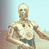 Static pixelated image of a humanoid robot with metallic gold and brown tones, standing against a light blue background with vertical gray stripes on the left.
