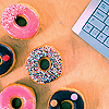 A top-down view of six donut-shaped icons with various toppings on a light brown surface, next to a partial keyboard.