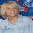 Pixelated static image of a person with light brown hair smiling, wearing a white top against a blue and gray background.