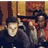 Pixelated static image of two people in a dimly lit interior with warm tones and visible dithering patterns.