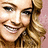 Pixelated close-up of a smiling person with light brown hair tied back, wearing dark clothing against a pink background.
