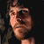 Pixelated close-up of a person's face with light skin tone, dark hair, and a neutral expression against a dark background.