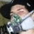 A person wearing a black hat and white mask with green accents, holding a camera-like object near their face.