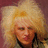 Pixelated close-up of a person with voluminous blonde hair against a maroon background, wearing dark clothing.