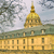 Pixelated image of a large building with a golden dome and spire, set against a cloudy sky with trees on the left.