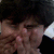 Pixelated close-up of a person with dark hair and light skin, hands near face, dark clothing, and a bright light source on the right.