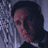 Pixelated static image of a person with dark hair and light skin leaning against a textured wall, wearing a dark top with a white collar.