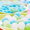 A static image of a tray holding multiple round, pastel-colored candies with blue and green swirls, set against a blurred background of similar candies.