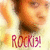 A pixelated image of a person with short dark hair wearing a light-colored top, with the text "ROCKIN!" in red below.