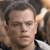 A pixelated close-up of a person with short dark hair, light skin, and a neutral expression, wearing a dark shirt with a white collar.