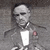 Two identical grayscale figures in formal attire with white bow ties and dark suits, positioned side-by-side against a textured gray background.