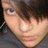 Pixelated close-up of a person's face with light skin, dark hair, and visible earlobe showing small earrings.