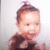 Pixelated image of a child with short brown hair wearing a dark brown top against a light gray background.