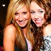 Two women with long hair pose closely together, smiling at the camera in a static image.