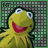 Yellow frog puppet with large white eyes and red mouth, smiling against green background with pixelated text