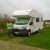 Pixelated static image of a white recreational vehicle on grass with a blurred background.
