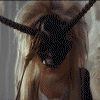A person with long blonde hair wears a black horned mask that shifts position , revealing their face in some views