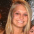 A blonde woman with shoulder-length hair smiles broadly, showing teeth, against a dark background with light speckles.